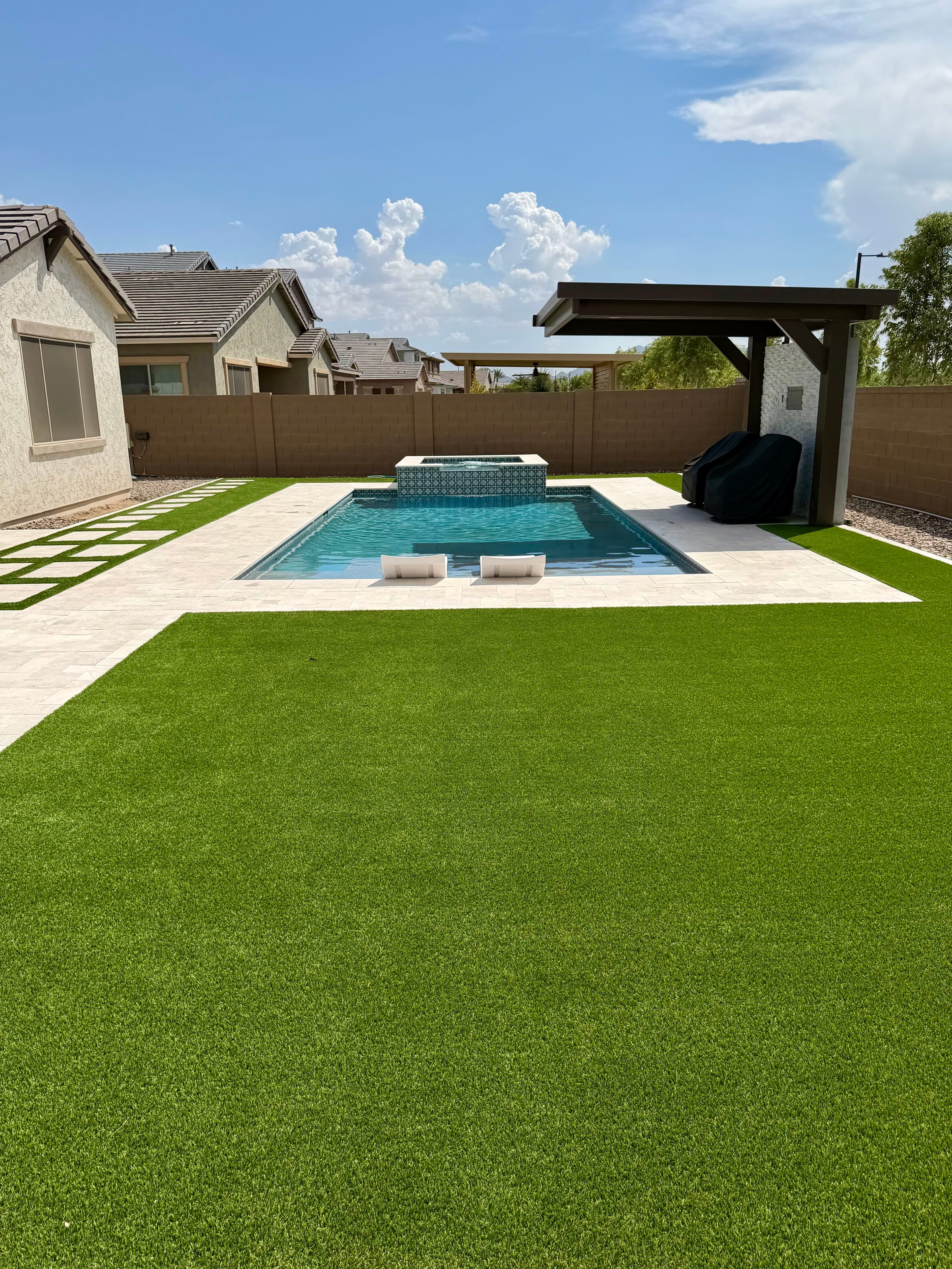 Artificial turf, pavers, and travertine installed around a backyard pool by Nice Turf.